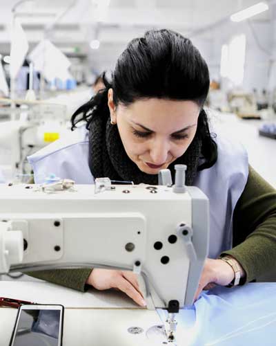 Mulher esta em uma confecção trabalhando em uma máquina de costura industrial.