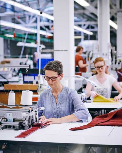 Mulher trabalhando em confecção e costurando em máquina reta industrial.