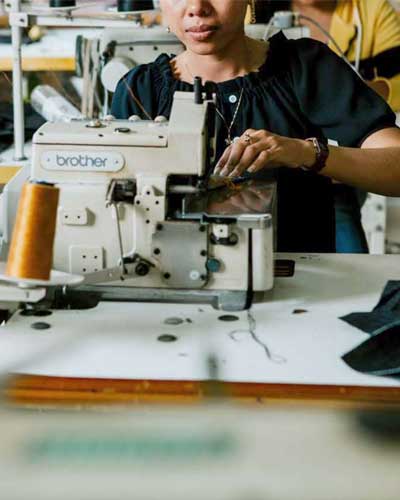 Mulher trabalhando em confecção e costurando em máquina reta industrial.