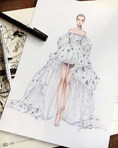 Mulher sentada em frente um notebook e desenhando manualmente croqui de moda.