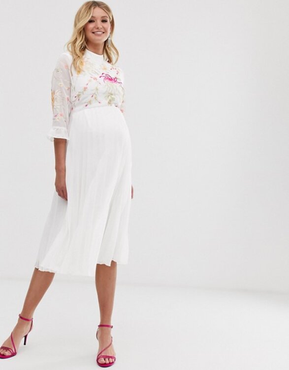 Vestido de noiva com saia midi plissada, corpo bordado floral colorido bem suave, gola alta e mangas 7/8 com babados. Mulher loira gravida com lindo sorisso, vestido de noiva com saia midi plissada, corpo bordado floral colorido bem suave, gola alta e mangas 7/8 com babados.