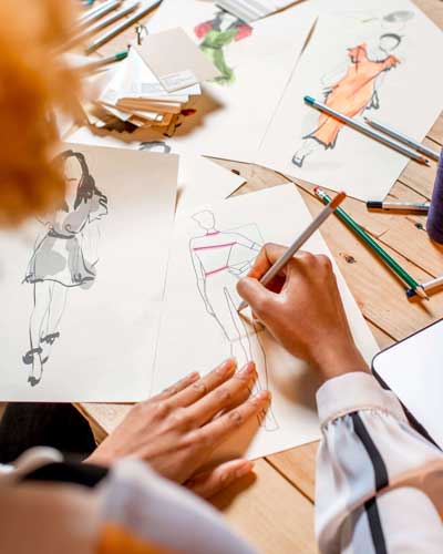 Mulher sentada em frente um notebook e desenhando manualmente croqui de moda.