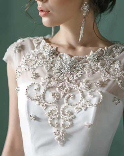 Mulher fazendo bordado em pedrarias em vestido.