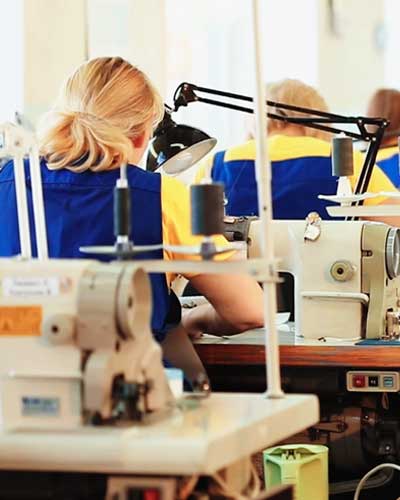 Mulher esta em uma confecção trabalhando em uma máquina de costura industrial.