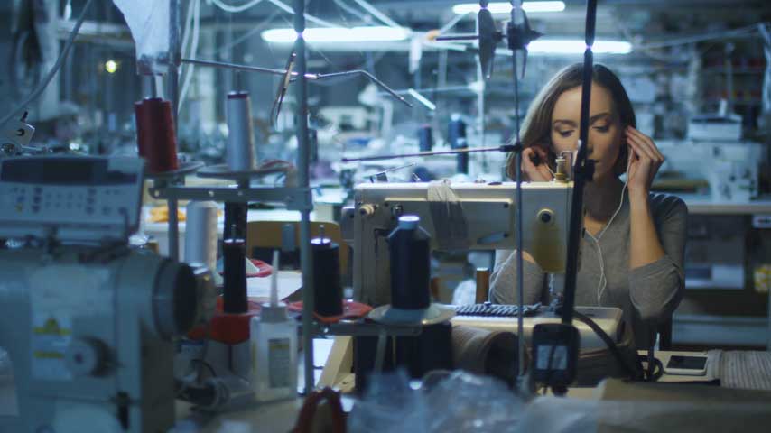 Mulher esta em uma confecção trabalhando em uma máquina de costura industrial.